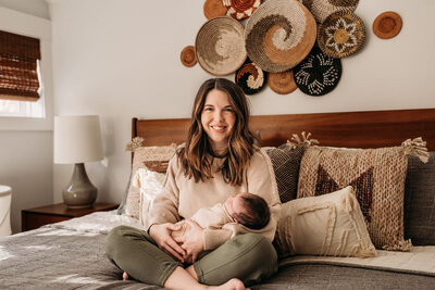 Mom sitting in a bed with her newborn with a boho wall decor in the background