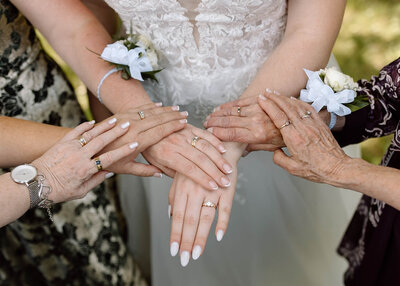 A generational photo of hands; the bride's hand is in the middle surrounded by her Mother, Grandmother and Aunts hands.