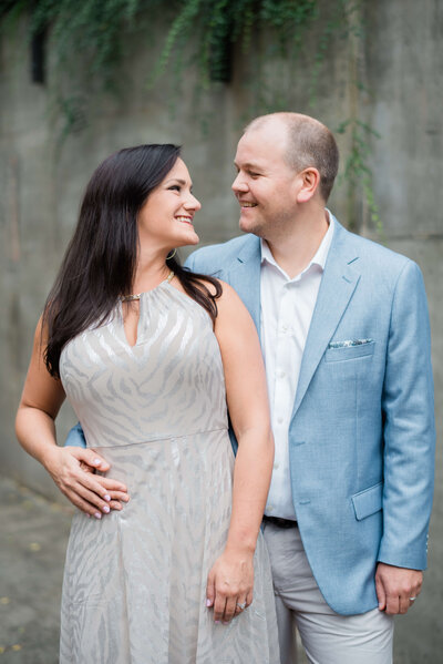 Girl in silver dresses looks lovingly at her fiance in a blue blazer during their engagement downtown photography session