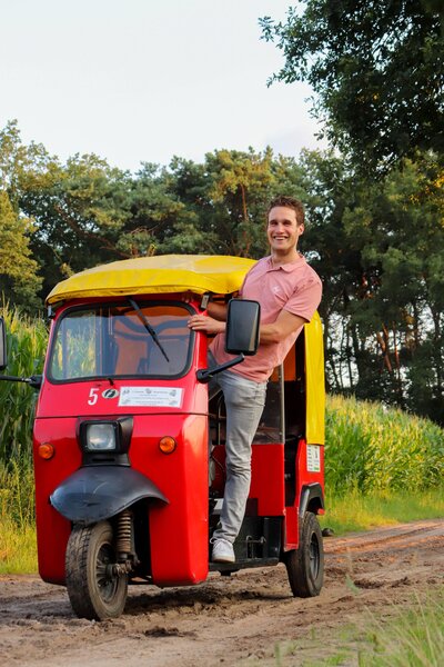 Man stapt in een rode TukTuk tijdens een groepsuitje door het Twentse landschap – ideaal voor een ontspannen activiteit met vrienden of collega’s.