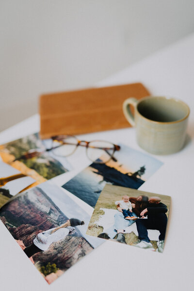 A mug, glasses, and printed photos laying on a white table