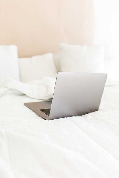 A picture of a macbook sitting on a bed and the screen is open and this is a stock image for the bookkeeping template for creatives by Dolly DeLong Education