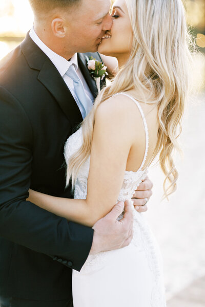 groom and bride kissing on dock by lake