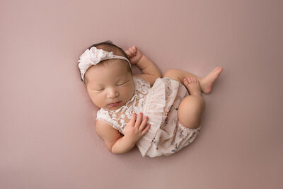 sleeping newborn baby posed on red blanket in white outfit and headband
