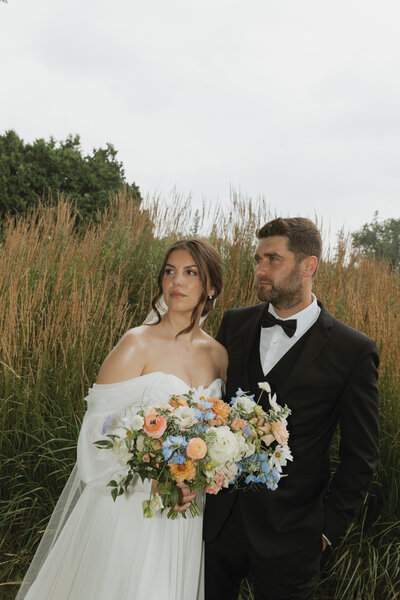 A bride and groom stand together at sunset, the bride holding a beautiful bouquet.