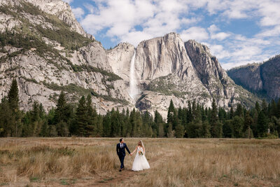 A bride and groom stand in front of a pristine alpine lake while holding their golden retriever dog. 