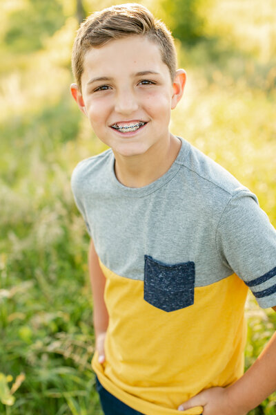 A white boy wearing a gray and yellow shirt smiling at the camera