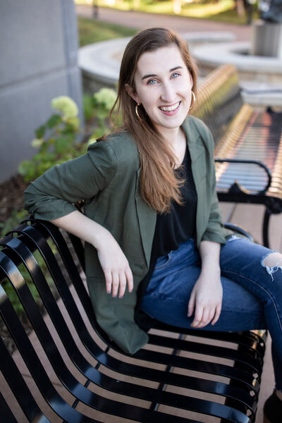 Mary Cait McManamon sitting on a bench outside wearing blue jeans and a dark green balzer