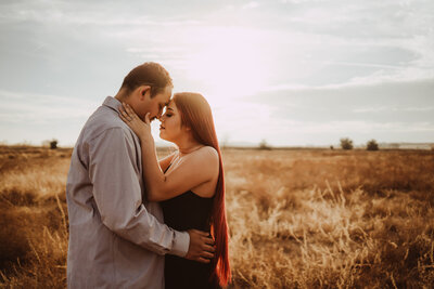 A couple facing each other, foreheads touching embracing on open golden field in fresno during sunset.