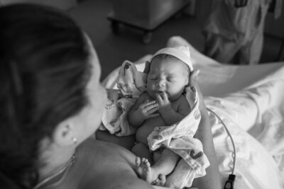 A new mother is holding up her baby to inspect it after being born