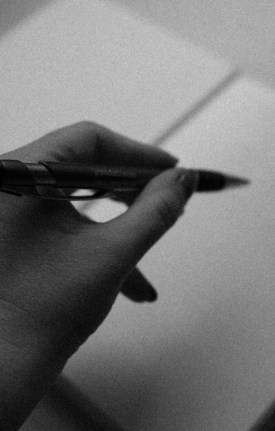 Black and white close-up of a hand journalling with a pen, representing Belief Coding® mindset work.
