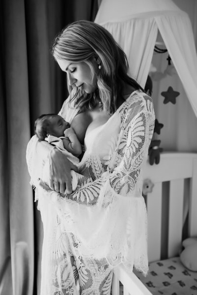 Black and white photo of mother in lace robe nursing newborn