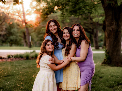 A mom and her girls hug for a photo in sunsete.