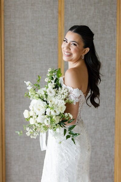 A person in a wedding dress holding a bouquet of flowers while looking over their shoulder and smiling 