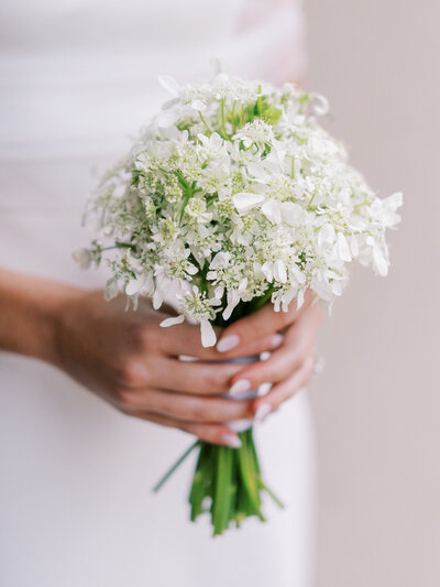 Bride's hands holding a small white flower bouquet