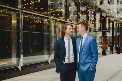 Two grooms with their arms around each other smiling at each other 