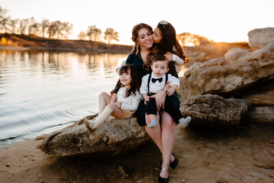 family photographer mom and three kids sitting on a rock by the lake interacting and hugging