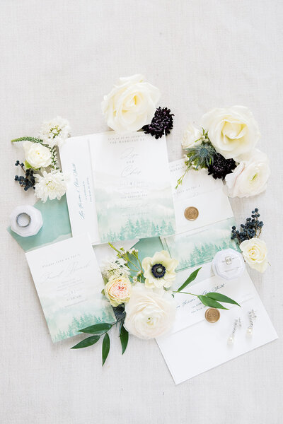 white background with flowers surrounding invitations laying flat