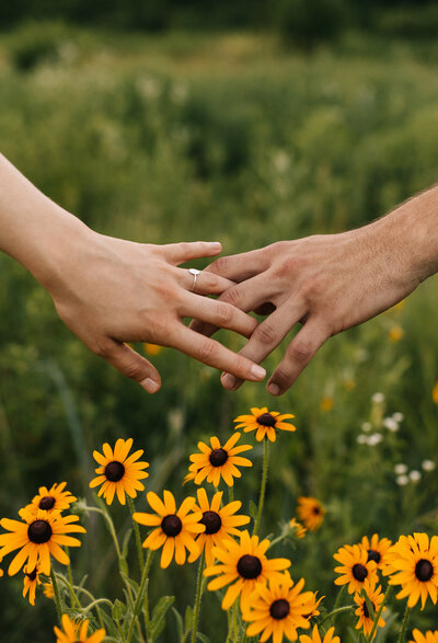Couple's fingers locking with flower field in background