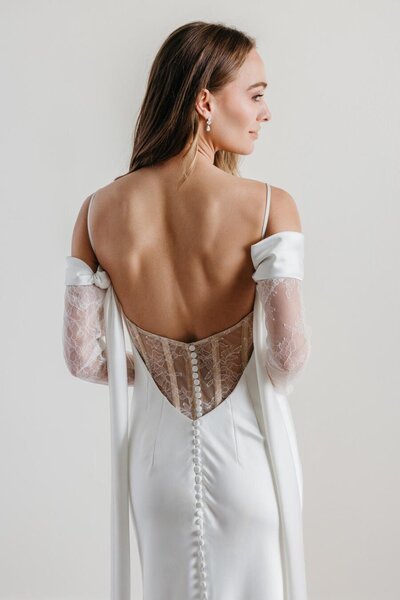 Bride in a satin gown with open back and sheer lace sleeves.