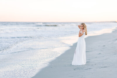 Senior girl in white dress looking over shoulder during sunset photo session on Sullivan’s Island beach in South Carolina[[[[