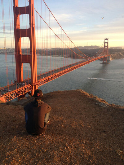 A man sits on a cliff overlooking the golden gate bridge
