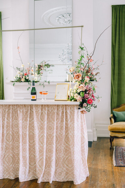 Floral-decorated table with champagne, mirror backdrop.