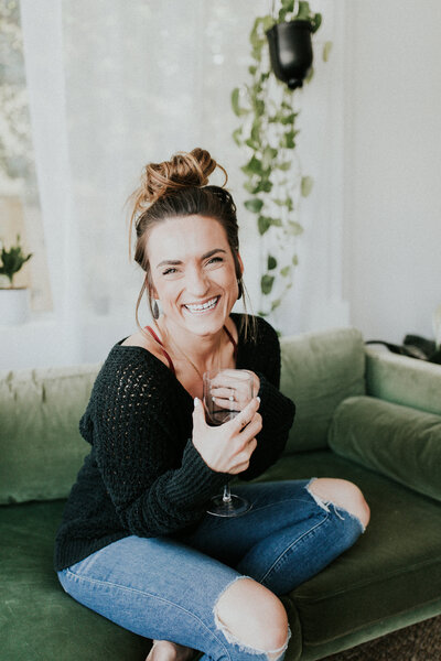 A woman photographer holds a glass of wine and smiles at the camera