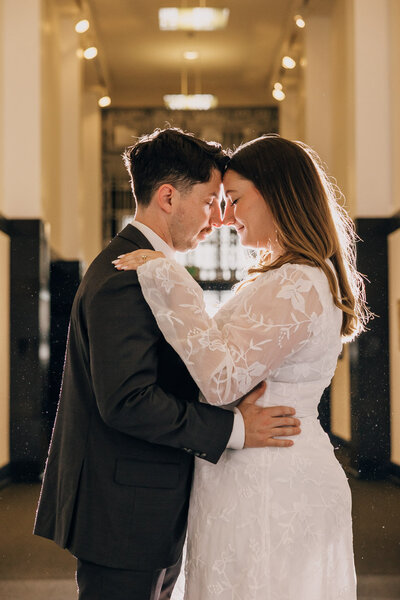 Couple standing forehead to forehead, embracing each other in the hallway of an art gallery.