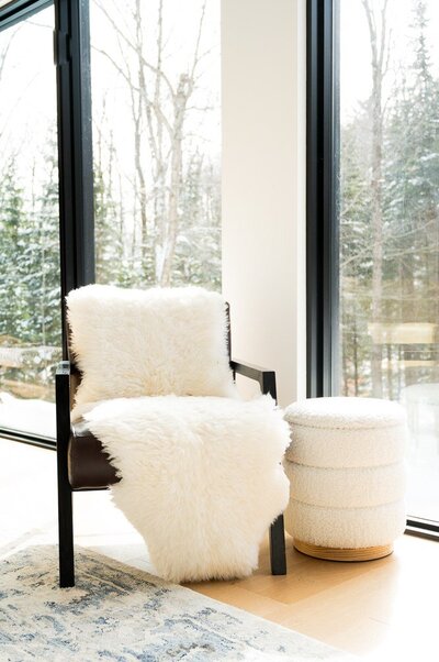 A cozy chair draped with a soft sheepskin, positioned in front of a bright window, inviting warmth and comfort.