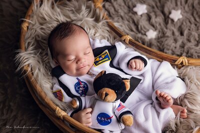 Newborn baby in a nasa astronaut outfit peacefully sleeping with a teddy bear by his side, creating a serene and adorable scene, captured during an in home newborn session in Orlando,Florida.