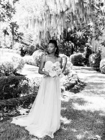 Black and white etherial photo of a bride standing among  tall grasses wearing Tadashi Shoji.