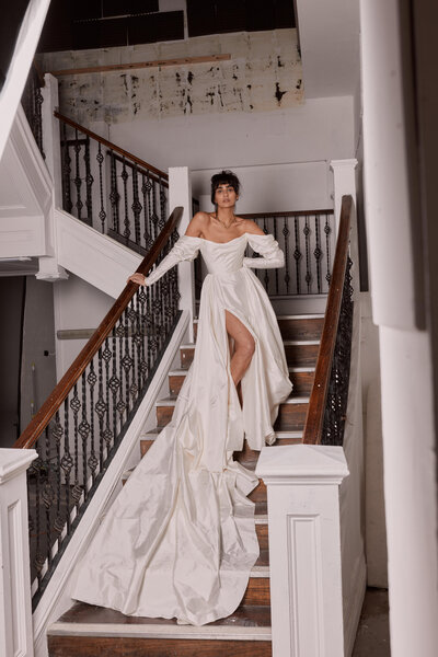 Handmade british long wedding dress in Italian silk with long-train worn on bride on staircase