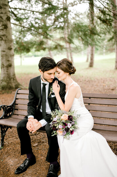 Bride and groom on a park bench. bride holding flowers leaning into groom
