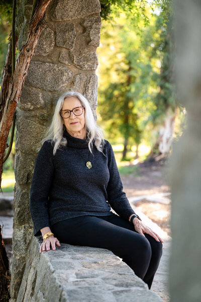 Audrie Meyer sitting peacefully by a stone wall, providing spiritual guidance for healing and transformation.