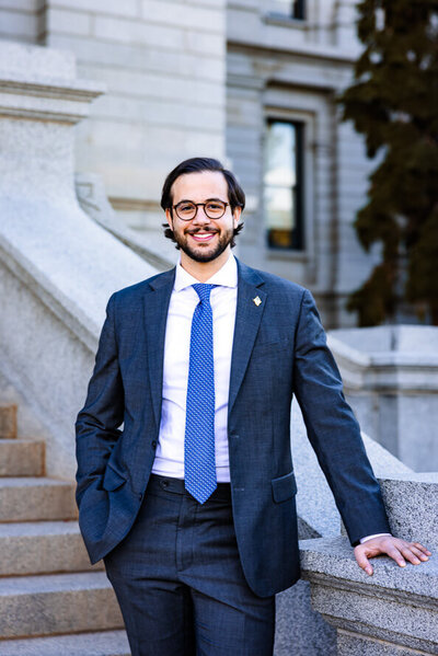 Man in blue jacket and blue tie hold onto edge of stairs at the Denver Capitol Building.