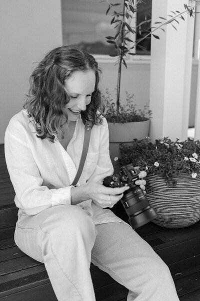 Jessica Anne, in-home newborn and family photographer based in Brisbane, smiles at the back of her camera while looking at photos from a recent photoshoot.