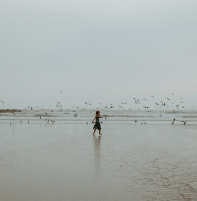 girl walking on beach with birds flying around her