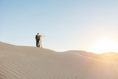 Bride and groom looking off into the distance during their elopement at the Little Sahara Sand Dunes in Utah, capturing a moment of love and adventure against a stunning desert landscape.