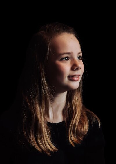 een blond tienermeisje dat opzij kijkt in portretstijl op een zwarte achtergrond