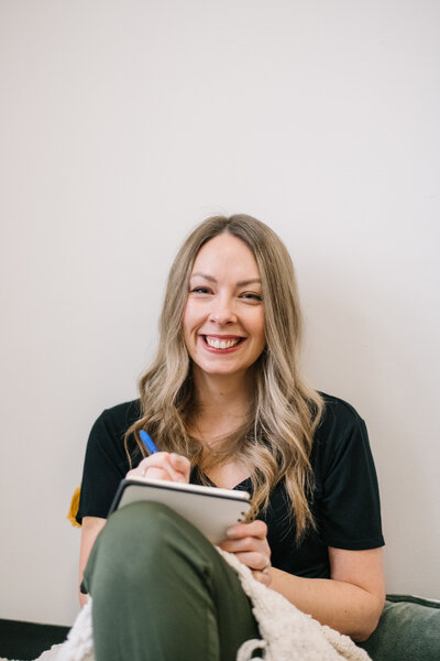 Sammy smiling sitting in front of a white wall writing in a notebook
