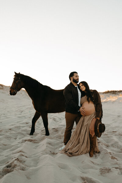 Expecting mother in earth-toned dress holding baby bump during soft, natural light maternity photography session – Mendham, NJ