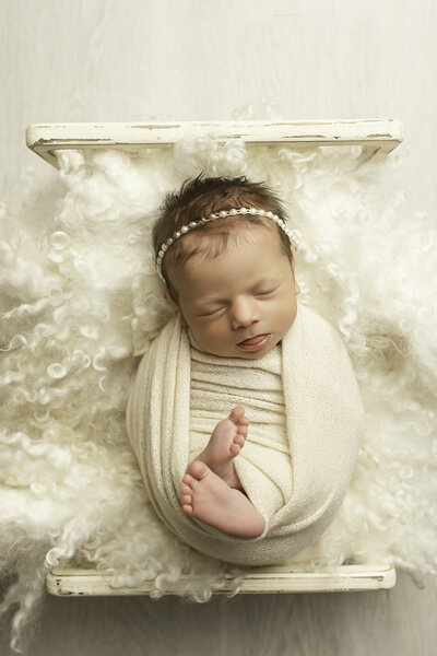 A precious baby girl peacefully laying in a wicker chair, wrapped in soft fabric, surrounded by a cozy setting, captured in a calm and adorable moment by Chunky Monkey Photography.
