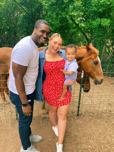 Iskra is happily posing for a photo with her family and a horse in the background.