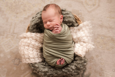 Newborn baby wrapped in cloth and laying in a basket.