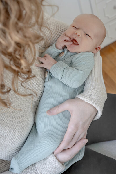 Lifestyle newborn photography session with two moms holding baby in cozy nursery with natural light— captured by Alliston and Barrie maternity, newborn, and family photographer.