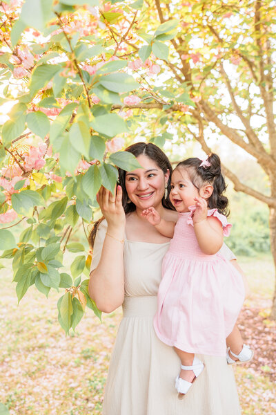 A mother and baby enjoying cherry blossoms during a portrait photography session, captured in soft natural light in Howard County, Maryland.