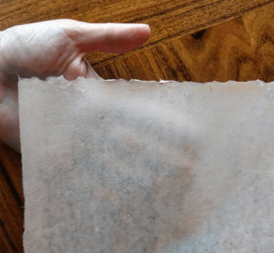 Hand holding a translucent sheet of handmade washi paper, highlighting its fibrous texture.