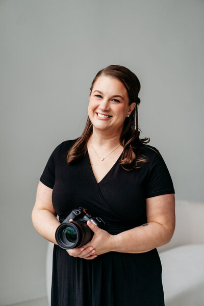 Female holding a camera and smiling.