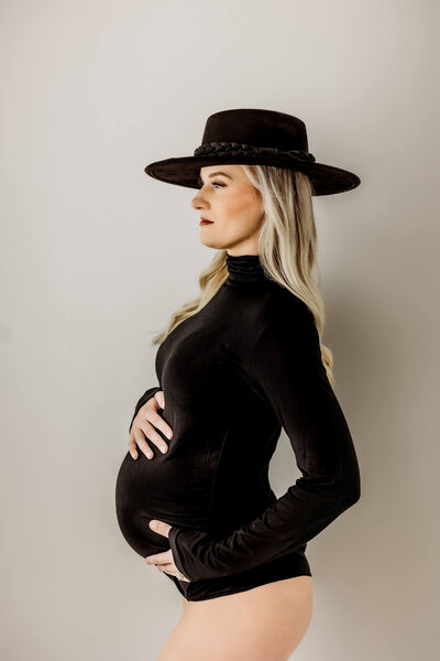 Studio portrait of young mother expecting baby in black maternity leotard and hat near Eau Claire